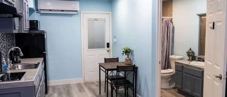 A compact kitchen with a dining area, a white door, and a bathroom with a shower curtain.