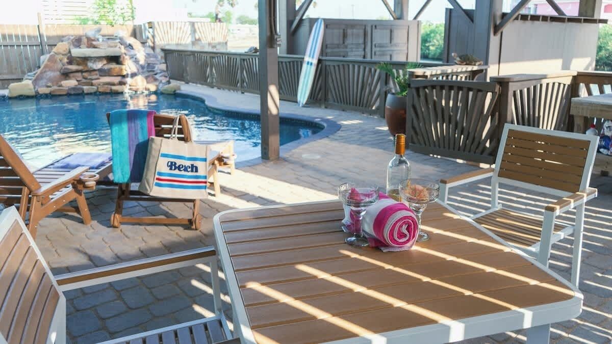 A poolside area with lounge chairs, a table with drinks, and a 'Beach' tote bag.