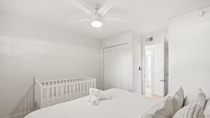 A bedroom with a white crib, a bed with white bedding, a ceiling fan, and a walk-in closet. - Central Cozy Home | Free Crib & Parking Space (Tampa)