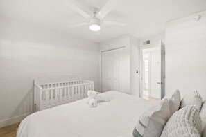 Ein Schlafzimmer mit einem weißen Babybett, einem Bett mit weißer Bettwäsche, einem Deckenventilator und einem begehbaren Kleiderschrank.