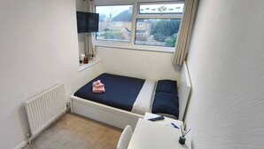 A small, single-bed room with a window, a desk, and a TV mounted above it. - Room-cosy Small Double Room in Quiet Sha (Chelmsford)
