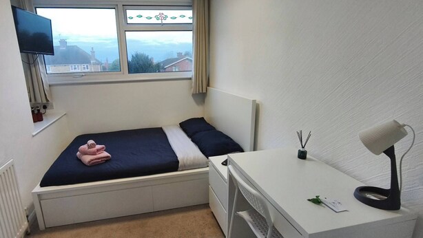 A small bedroom with a bed, a desk, a chair, a TV, and a window with a view of houses. - Room-cosy Small Double Room in Quiet Sha (Chelmsford)