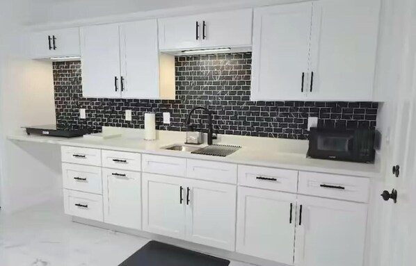 Une cuisine moderne avec des meubles blancs, un pare-feu noir et un four à micro-ondes encastré.
