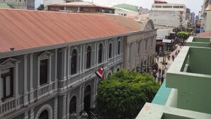 Vista de la calle con un edificio de ventanas arqueadas y tejado rojo.
