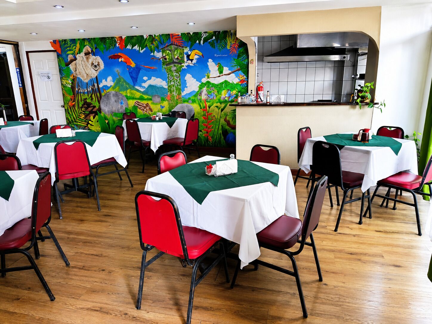 Un restaurante con varias mesas, sillas rojas y un mural de fauna tropical en la pared.