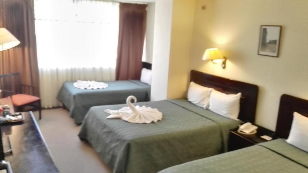Ein Hotelzimmer mit zwei Betten, einem Schreibtisch mit Lampe, einem Sessel und einem Nachttisch mit Telefon.