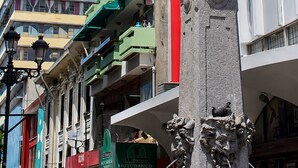 Vista de una calle con una destacada torre del reloj, edificios de varios pisos y un cielo azul despejado.