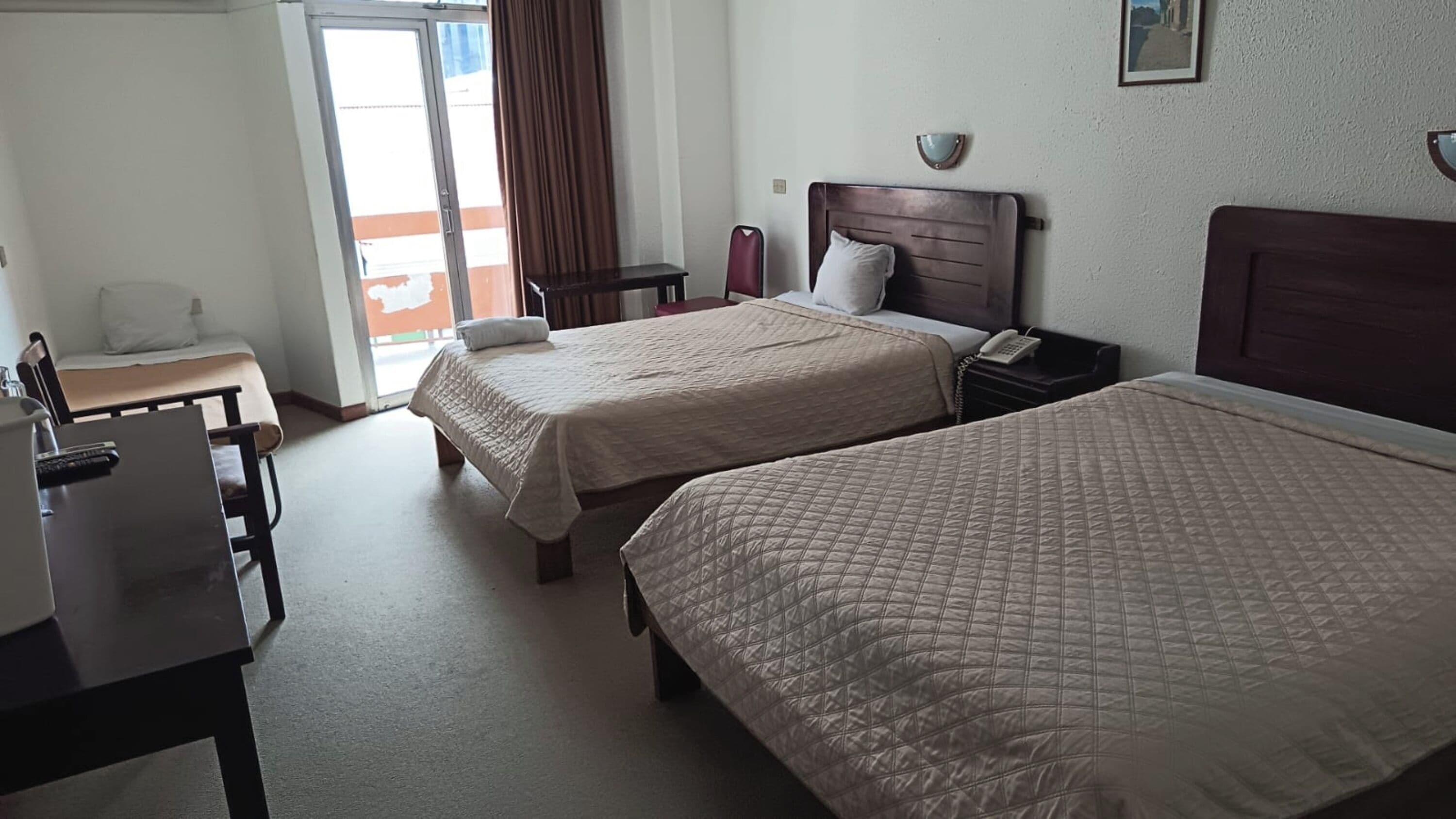 Habitación de hotel con dos camas, un escritorio, una silla, un teléfono y una ventana con cortinas.
