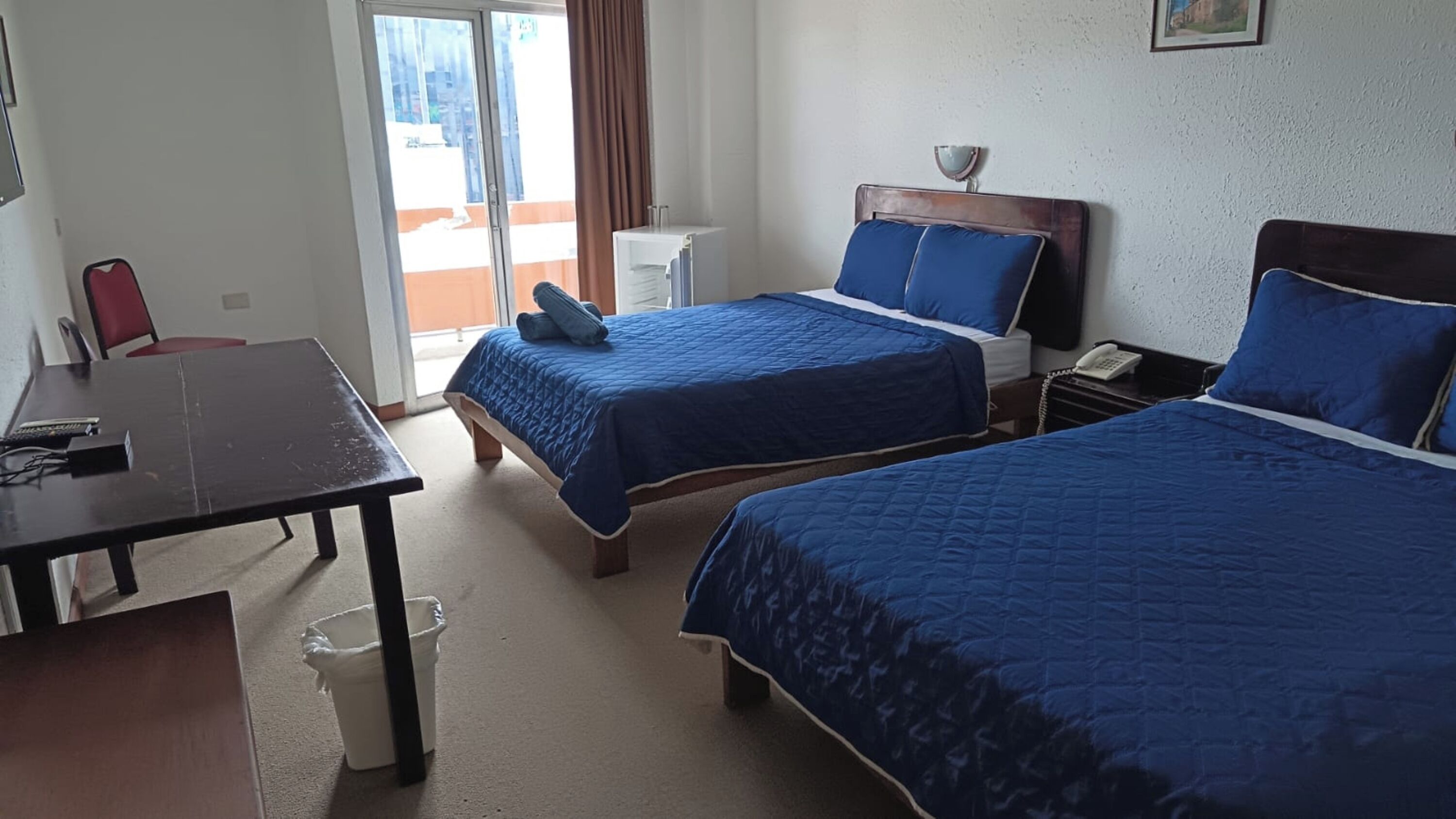 A hotel room with two beds, a desk, a chair, and a window with a view of the outside.