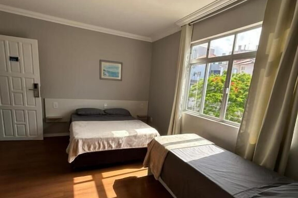 Una stanza con un letto, una finestra con tende, una porta e un quadro appeso al muro.