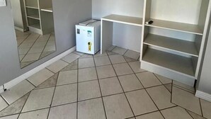 A room with a tiled floor, a white desk, a white wardrobe, and a small white heater. - sunset inn canasvieiras (Florianópolis)