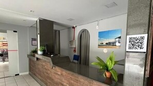 A reception desk with a wooden counter, a potted plant, a QR code, and a framed picture on the wall. - sunset inn canasvieiras (Florianópolis)