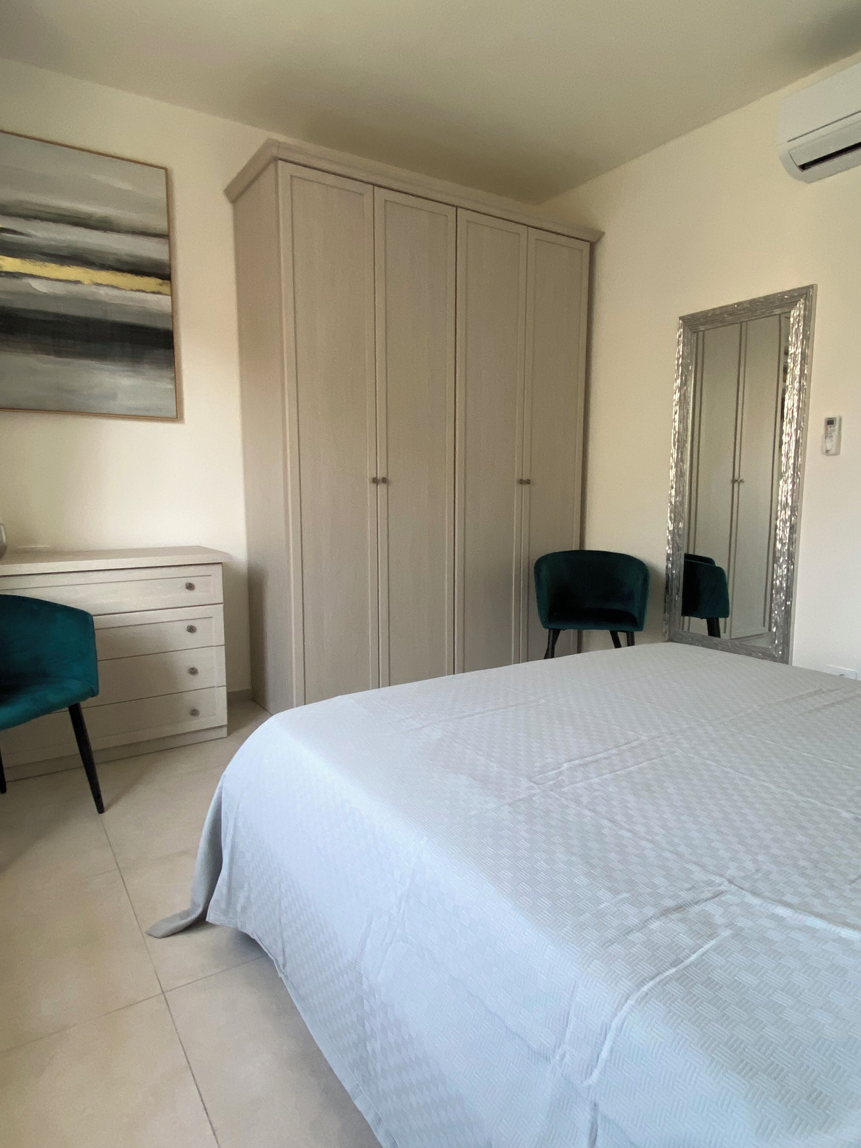 A bedroom with a bed, a dresser, a chair, a wardrobe, and a mirror.