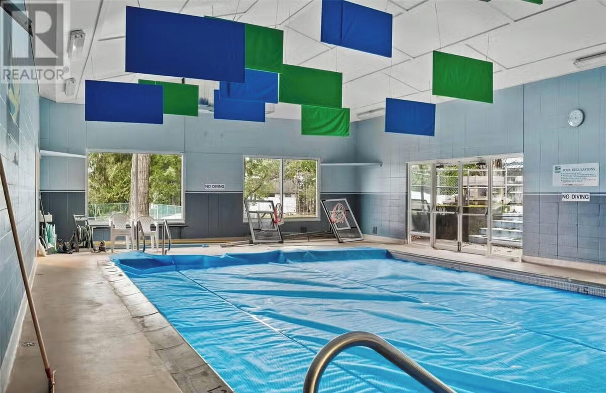 A swimming pool with a no diving sign, a basketball hoop, and a covered area with a bench.