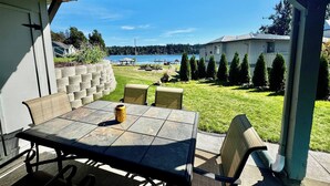 Un patio exterior con una mesa y sillas, vistas a un lago y un edificio al fondo.