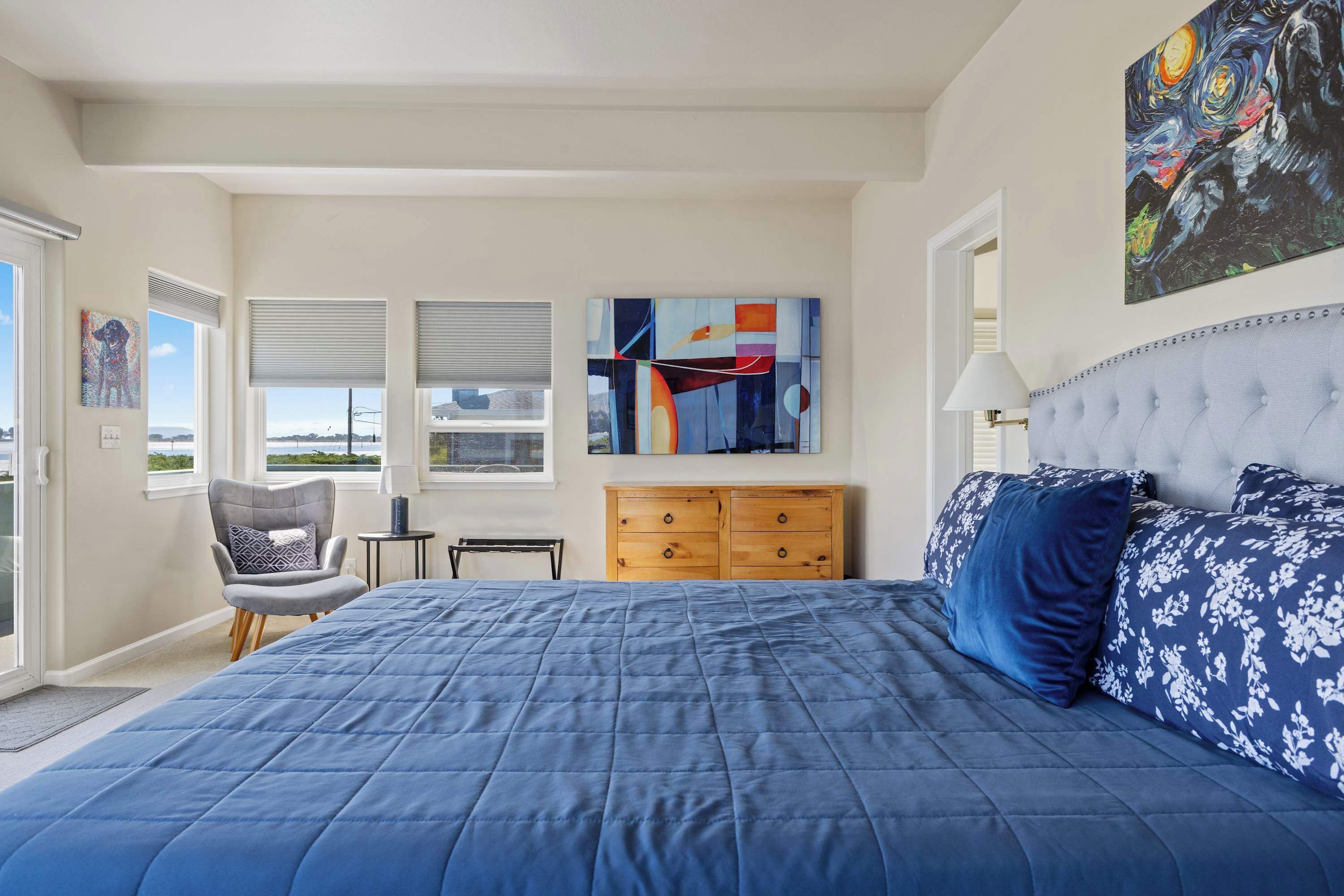 A bedroom with a large bed, a chair, a dresser, and artwork on the walls.