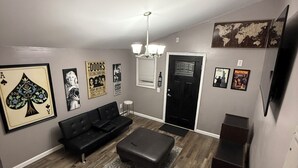 A modern living room with a black sofa, a wooden coffee table, and a black ottoman. There is a world map on the wall and a framed picture of a playing card. - Cozy home just a minute walk from the lake! (Tobyhanna)