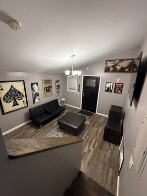 A modern living room with a black sofa, a wooden coffee table, and a black ottoman. There is a world map on the wall and a framed picture of a playing card. - Cozy home just a minute walk from the lake! (Tobyhanna)