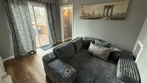 A cozy living room with a grey sofa, a painting of a bridge, and a string of lights. - Cozy home just a minute walk from the lake! (Tobyhanna)