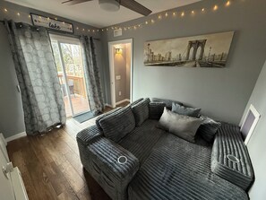 A cozy living room with a grey sofa, a painting of a bridge, and a string of lights. - Cozy home just a minute walk from the lake! (Tobyhanna)