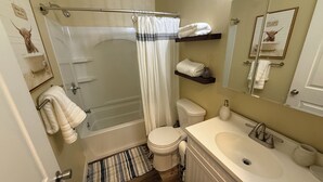 A bathroom with a shower, toilet, sink, and a mirror. - Cozy home just a minute walk from the lake! (Tobyhanna)