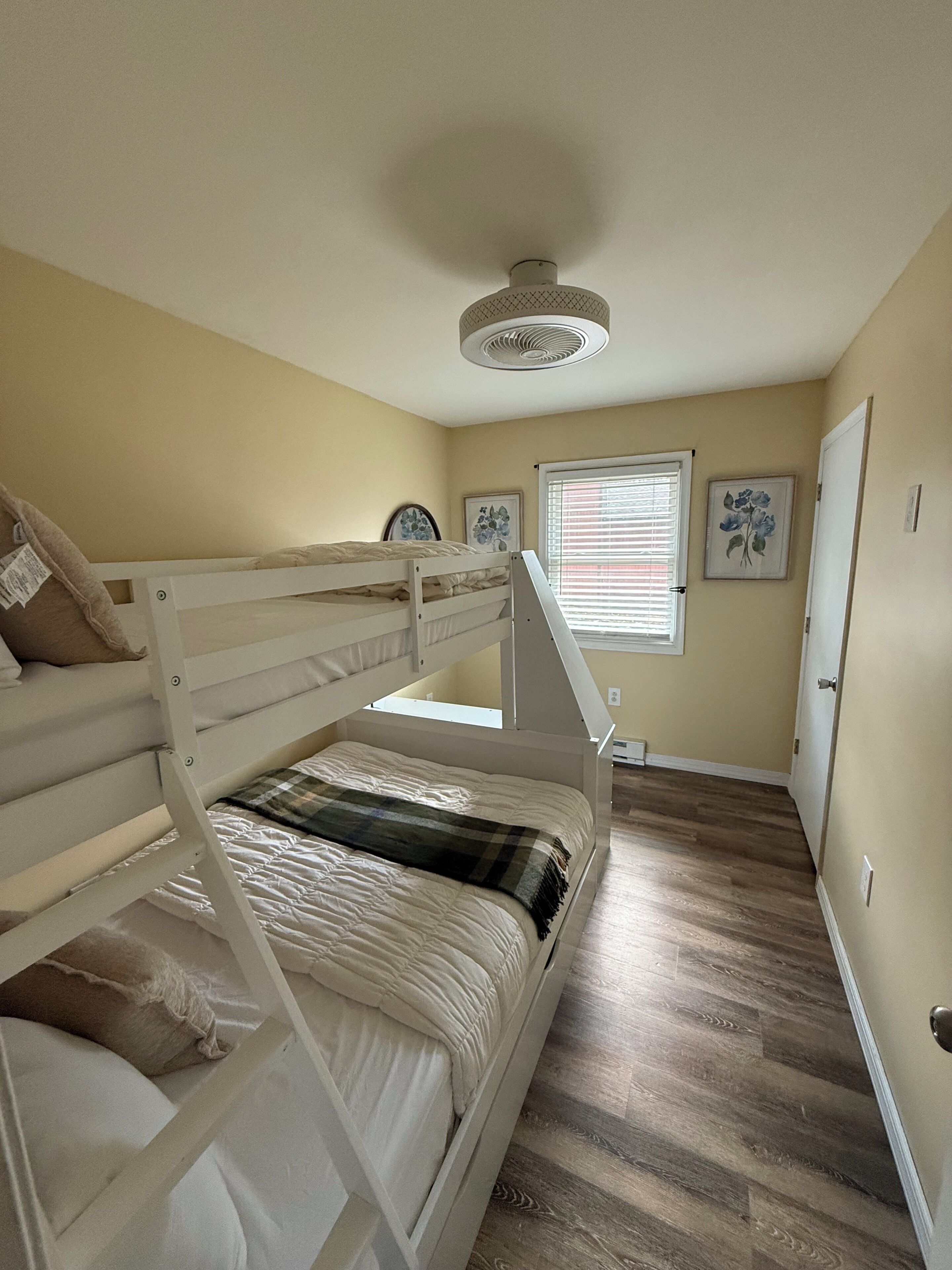 A bunk bed room with a ceiling fan, a window with blinds, and a door.