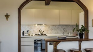 A kitchen with white cabinets, a tiled backsplash, a stove, an oven, a sink, and a bar area with stools. - 2-bedroom condo in peaceful Lucca with air conditioning and assigned parking (Lucca)