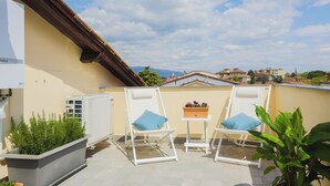 A rooftop terrace with two white lounge chairs, a small table with a flower pot, and a large planter with green plants. - 2-bedroom condo in peaceful Lucca with air conditioning and assigned parking (Lucca)