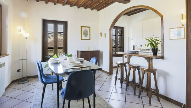 A dining area with a table set for four, blue chairs, a wooden ceiling, and a large mirror on the wall. - 2-bedroom condo in peaceful Lucca with air conditioning and assigned parking (Lucca)