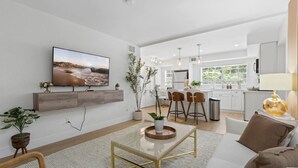 Een moderne woonkamer met een flatscreen televisie, een salontafel en een bank. Er is een keuken met een eethoek en uitzicht op de omgeving.