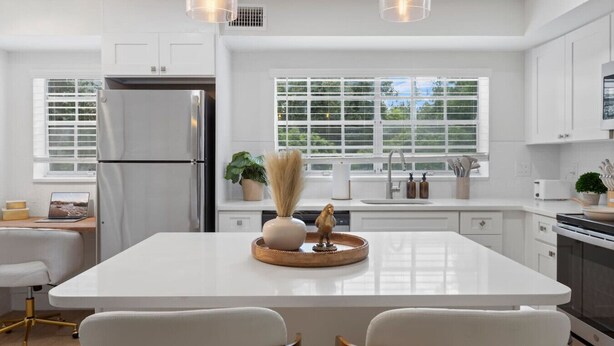 Een moderne keuken met witte kastjes, een centraal kookeiland en hanglampen.