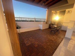 Uma varanda com piso de azulejos, mesa e cadeiras, e vista para a cidade.