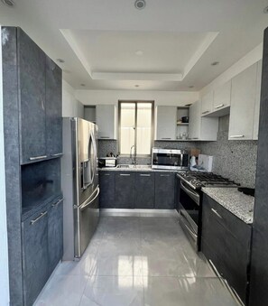 A modern kitchen with stainless steel appliances, dark cabinetry, and a large window. - 3-bedroom house in fantastic Santo Domingo Este with AC (Santo Domingo Este)