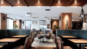Een modern restaurantinterieur met houten tafels, beklede zitbanken en hanglampen.