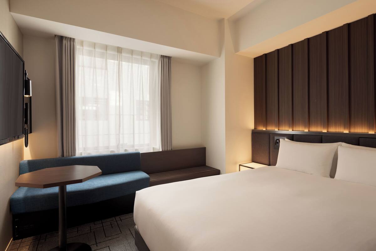 A hotel room with a bed, a sofa, a small table, a TV, and a window with curtains.