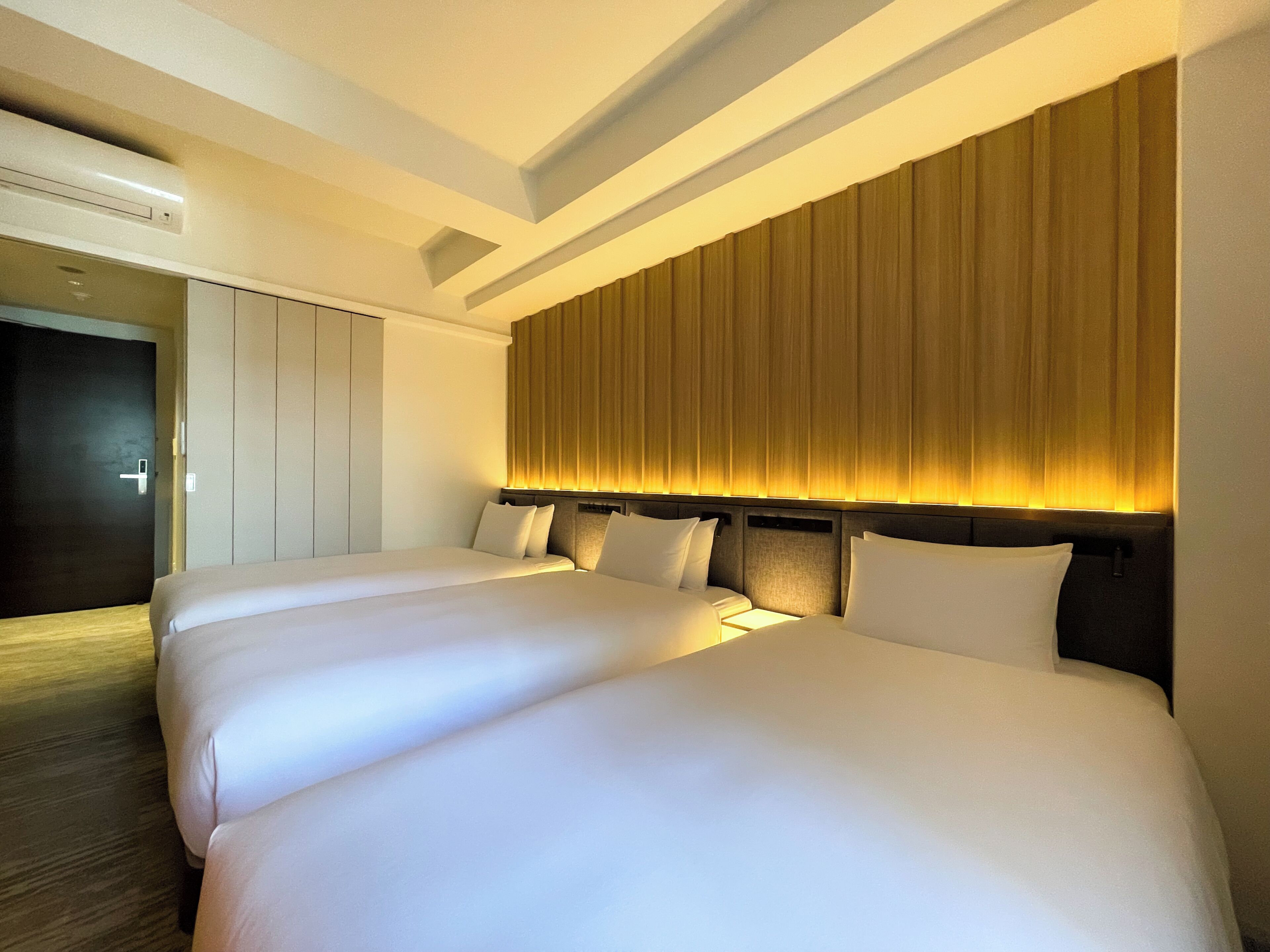 A hotel room with two beds, a dark door, and a wall with vertical blinds.