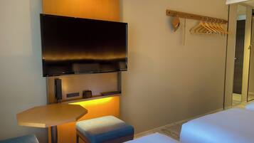 Una habitación de hotel con una televisión montada en la pared, una mesita, un banco y una cama.