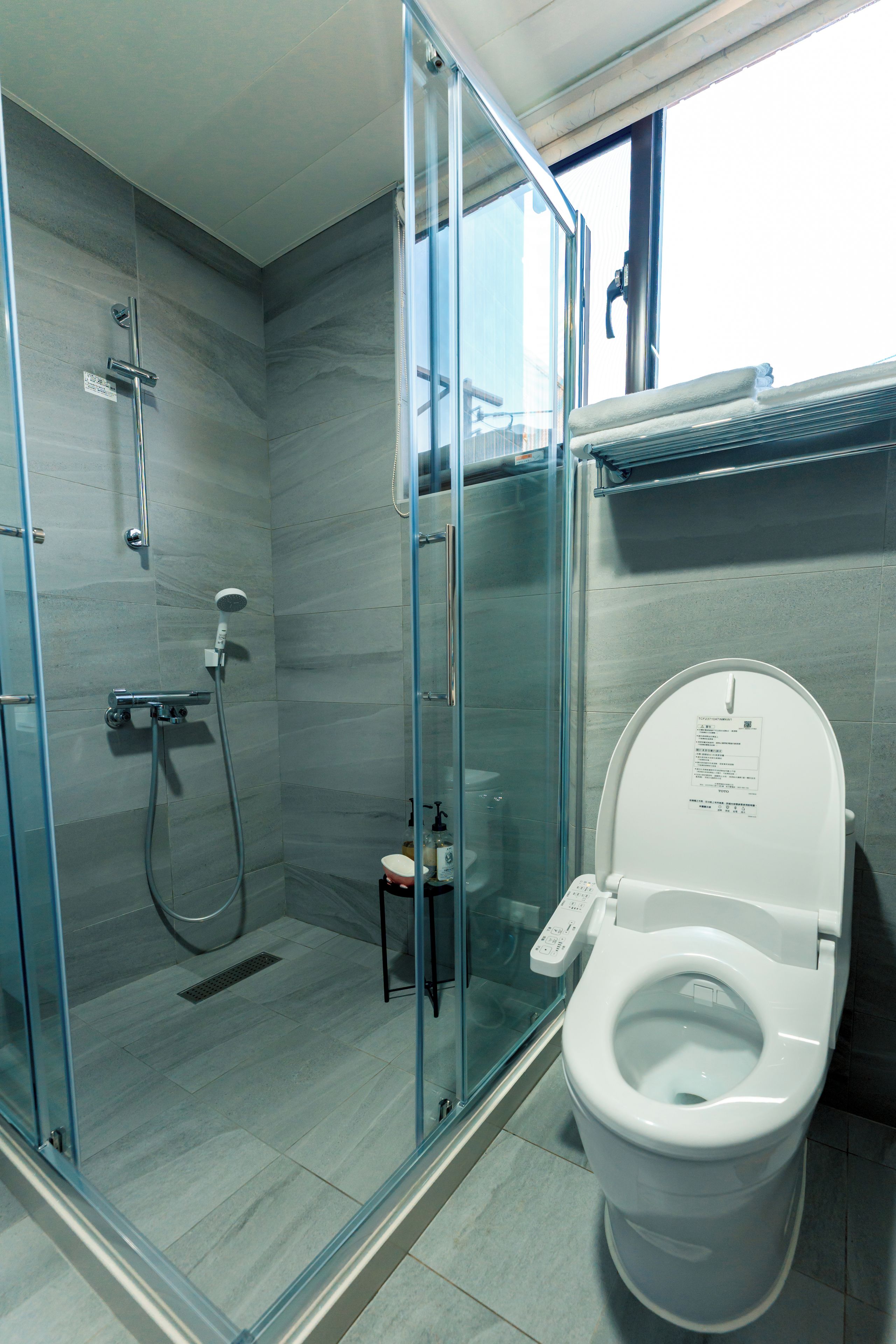A modern bathroom with a glass-enclosed shower, a toilet, and a small sink.