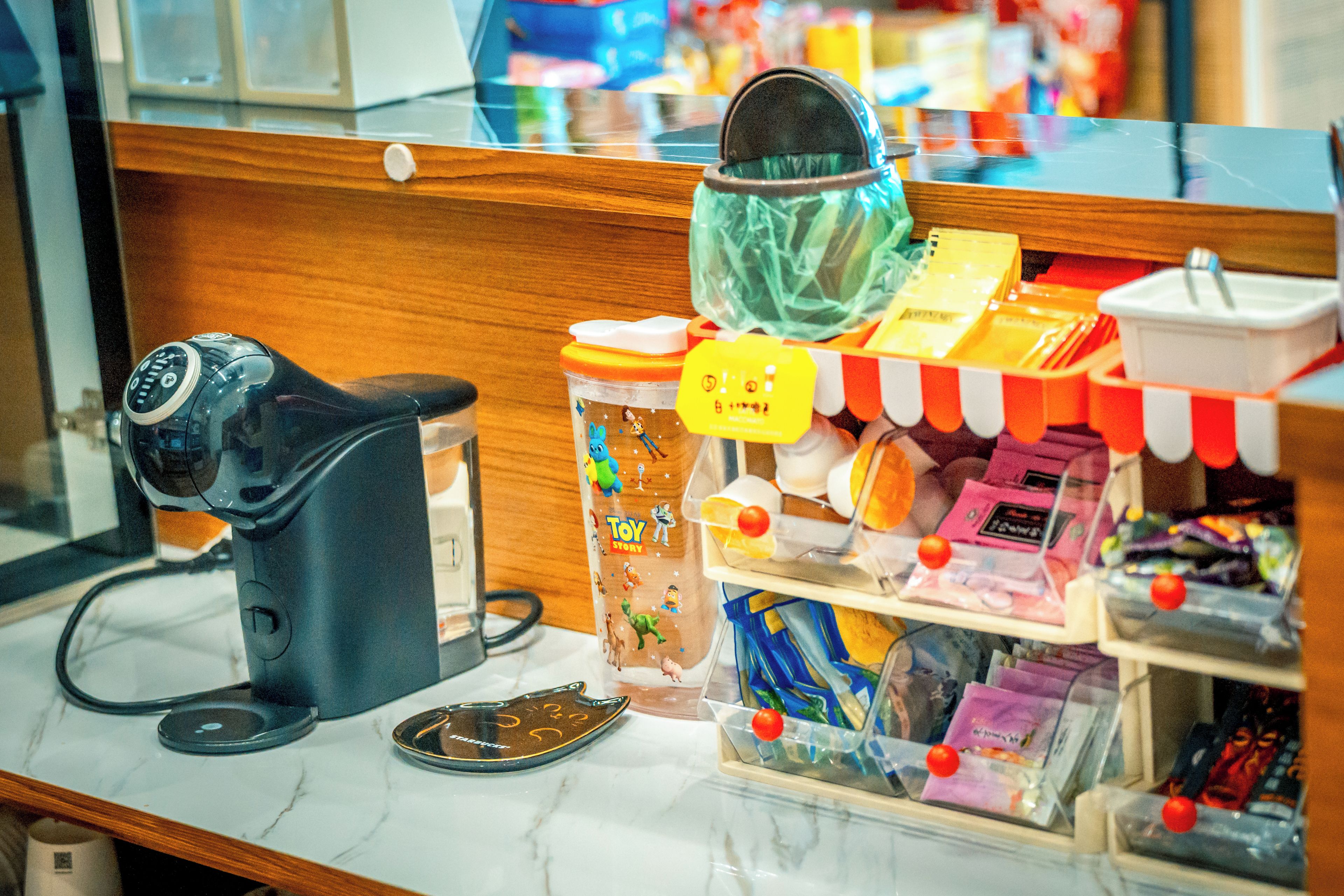 Un taulell amb una màquina de cafè, un recipient ple d'autoadhesius de colors i diversos objectes a les prestatgeries.