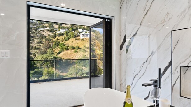 Un baño moderno con un ventanal grande, una bañera blanca, una botella de champán y una copa de vino.