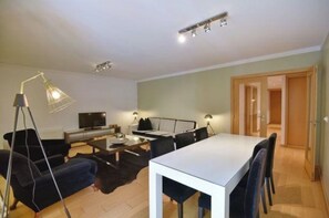 A modern living room with a white dining table, black sofas, a TV, and a lamp. - Modern 3BR House, Parque das Nações - Long Term (Lisboa)