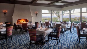 Un comedor con mesas y sillas, una chimenea y ventanas grandes con vistas.