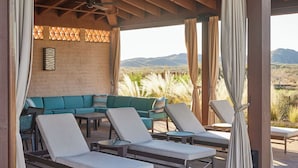 Un área de estar techada al aire libre con sillones reclinables y un sofá, techo de madera y vistas del paisaje.