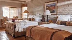 Habitación de hotel con dos camas, un ventanal grande con persianas, un cuadro colgado en la pared y suelo de madera.