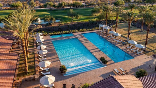 Piscina rectangular con sillas de descanso y sombrillas, rodeada de palmeras y vistas a un campo de golf.