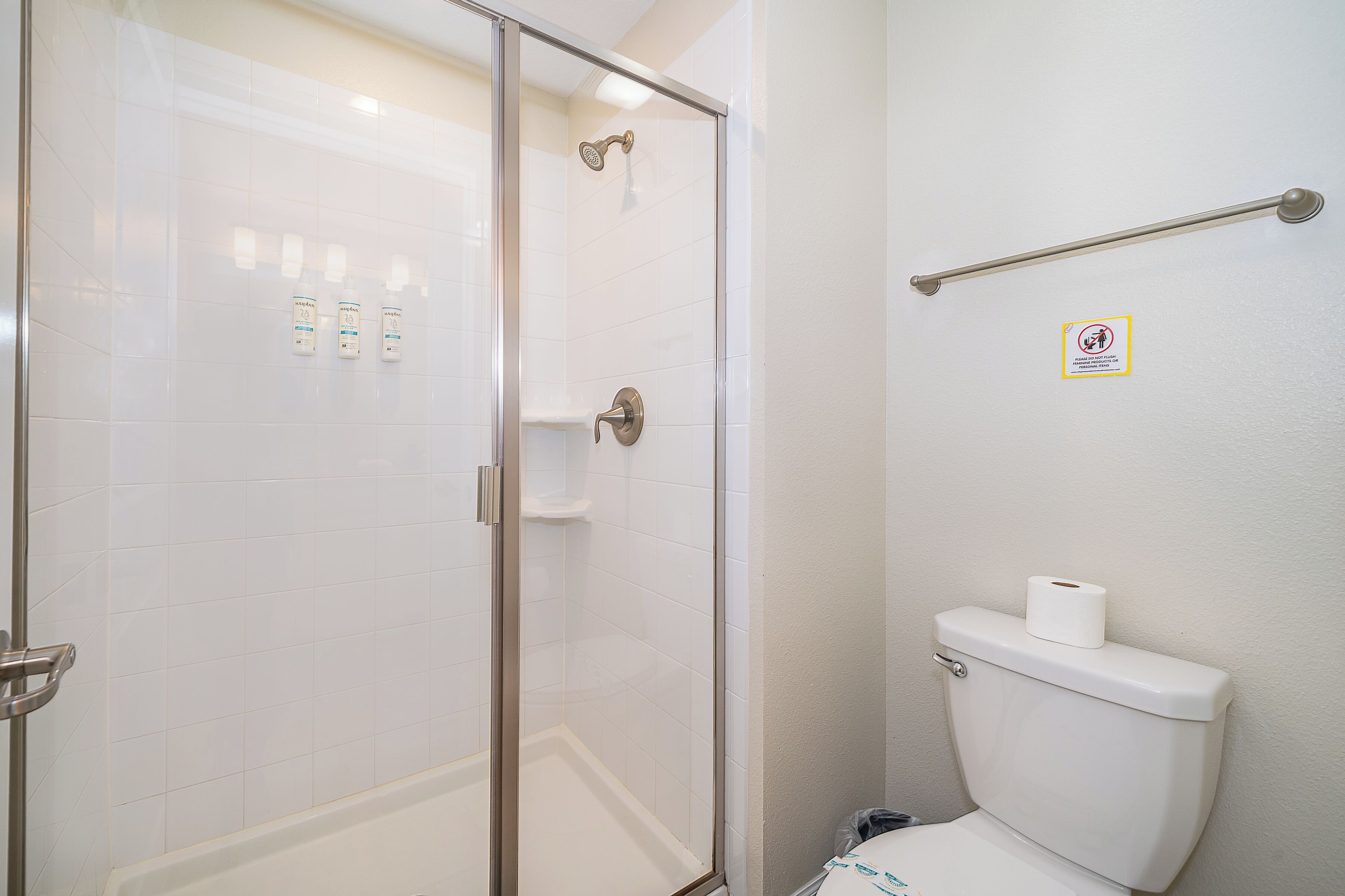 Un bagno con box doccia in vetro, un water e un corrimano a parete.