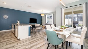 A modern kitchen with a built-in island, dining area with a white table and chairs, and a large sliding glass door to the outside. - Championsgate Blue Villa + Private Pool + Resort Access (Davenport)