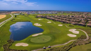 A golf course with sand bunkers, a pond, and a residential area in the background. - Championsgate Blue Villa + Private Pool + Resort Access (Davenport)