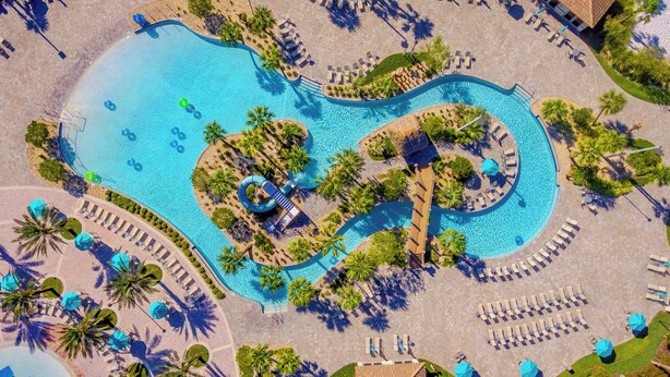 An aerial view of a resort with a large, winding pool surrounded by palm trees and sun loungers. - Championsgate Blue Villa + Private Pool + Resort Access (Davenport)