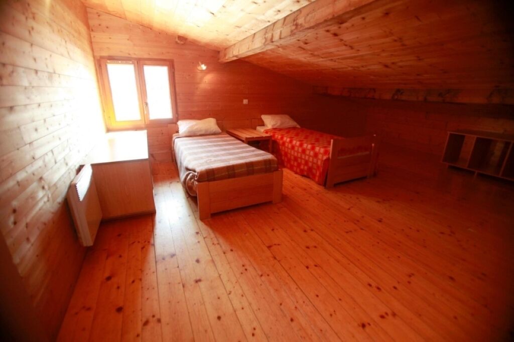 A single bedroom with a wooden floor, a bed, a small table, a radiator, and a window.
